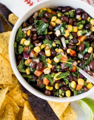 A bowl of black bean salsa with tortilla chips surrounding it.