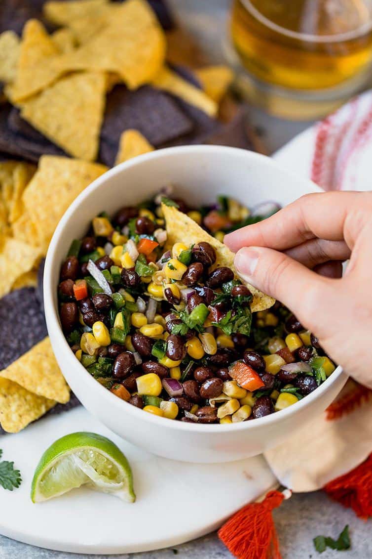 A hand dipping a tortilla chip into a bowl of black bean salsa