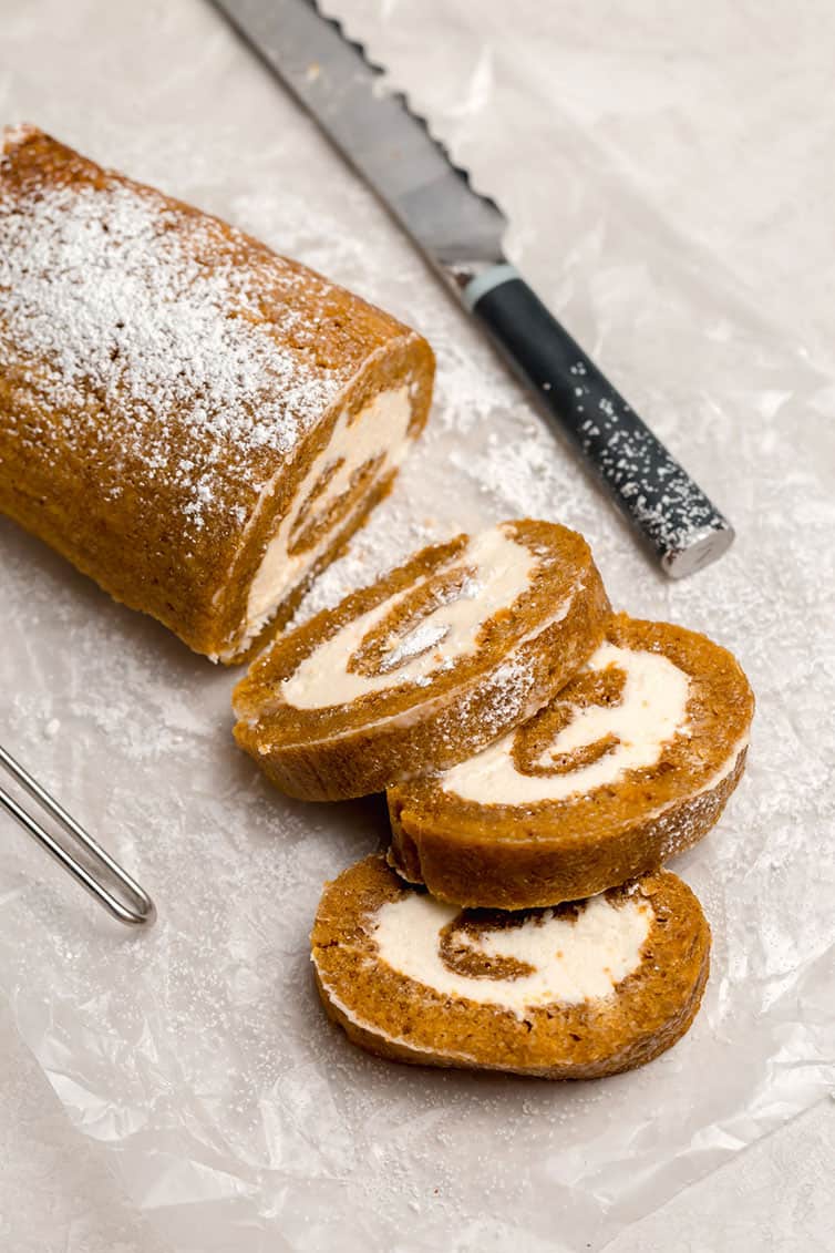 A pumpkin roll with three slices cut off on parchment paper.