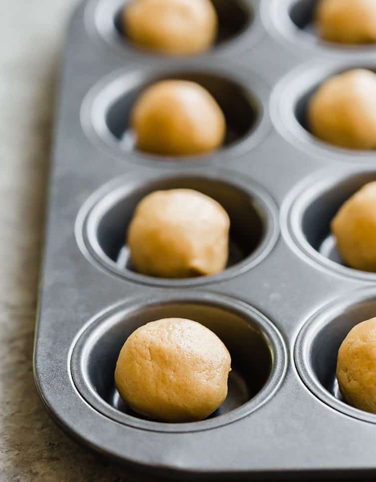 Balls of peanut butter dough in a mini muffin pan.