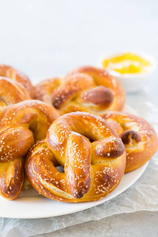 Soft pretzels on a plate with dipping mustard in the background.