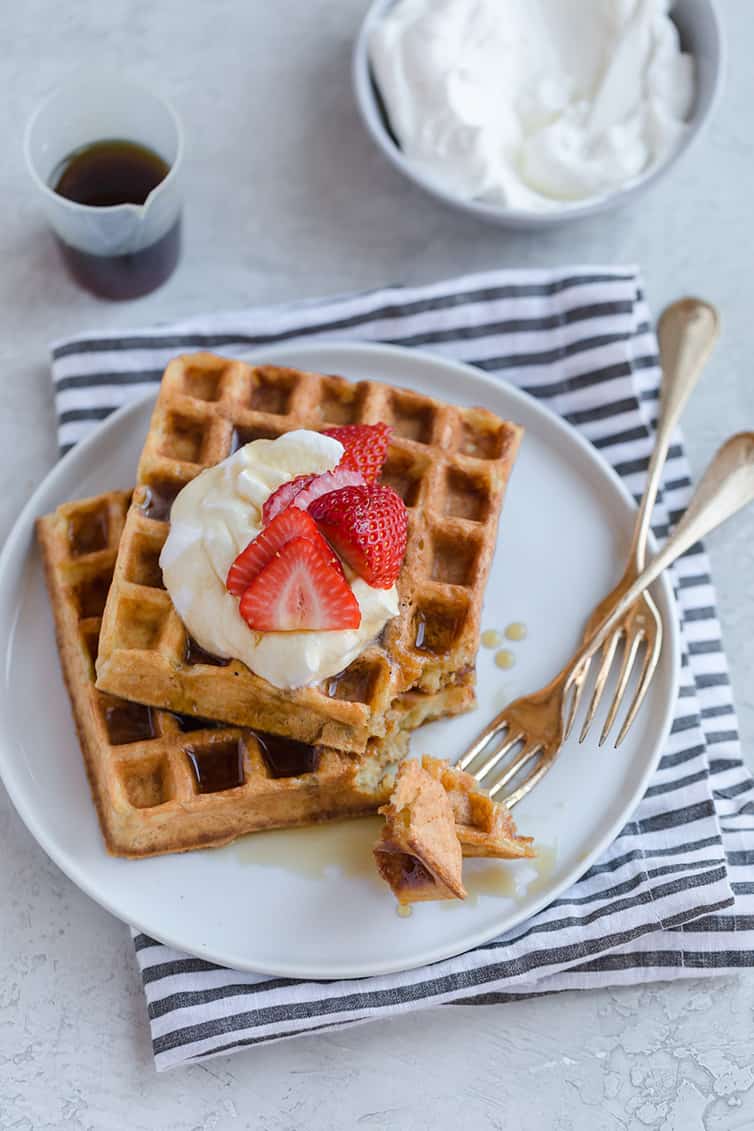 Overheat photo of two waffles on a plate with whipped cream and strawberries on top.