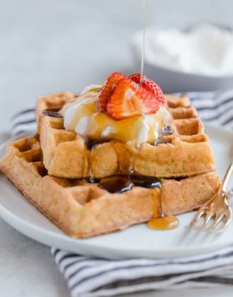 Two square waffles stacked with whipped cream and strawberries on top.