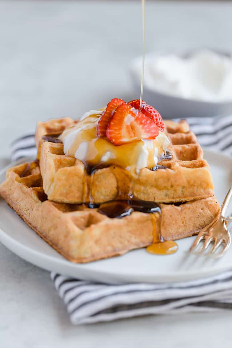 Two square waffles stacked with whipped cream and strawberries on top.