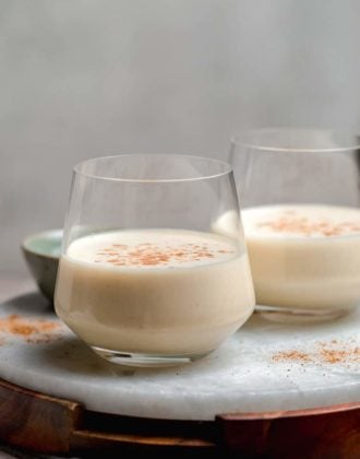 Two glasses half-filled with eggnog and a sprinkle of nutmeg.