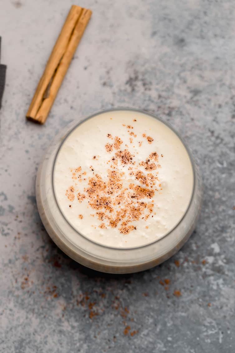 An overhead shot of a glass of eggnog with a sprinkle of nutmeg on top.
