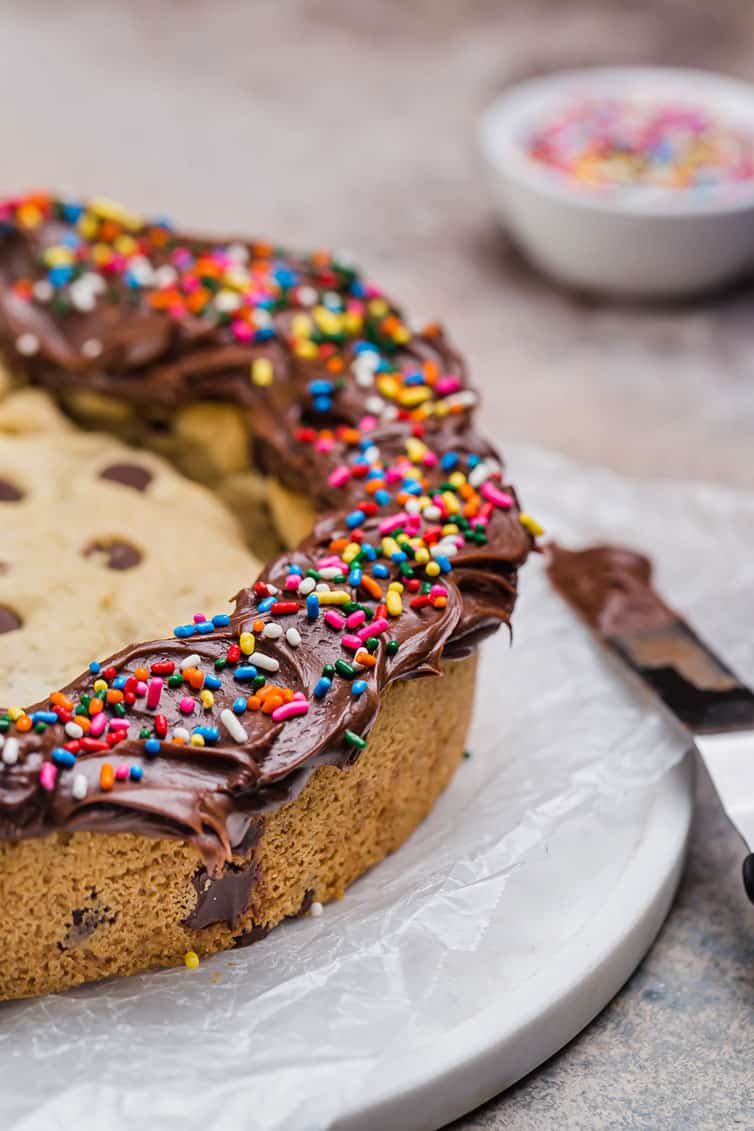A chocolate chip cookie cake decorated with chocolate frosting and sprinkles around the edges.