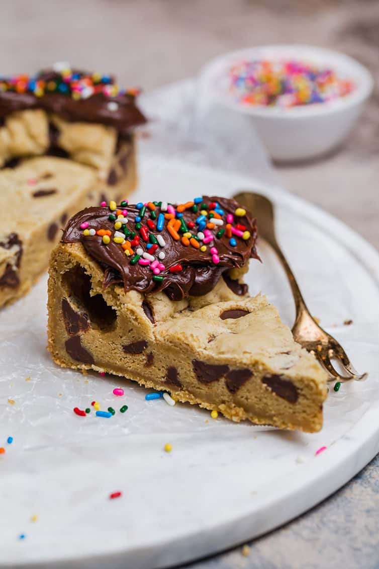 A slice of chocolate chip cookie cake with chocolate frosting and sprinkles along the edge.