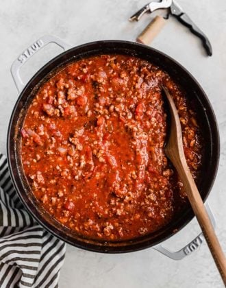 A large pot of meat sauce with a wooden spoon in it.
