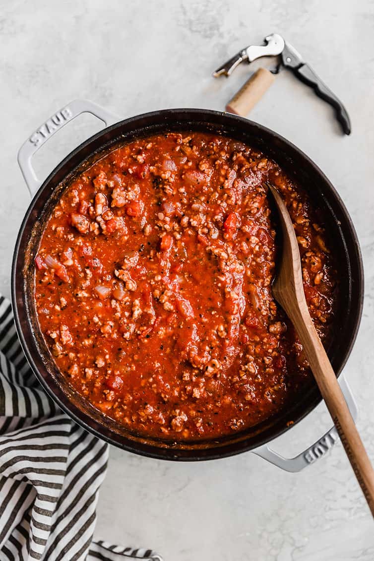 A large pot of meat sauce with a wooden spoon in it.