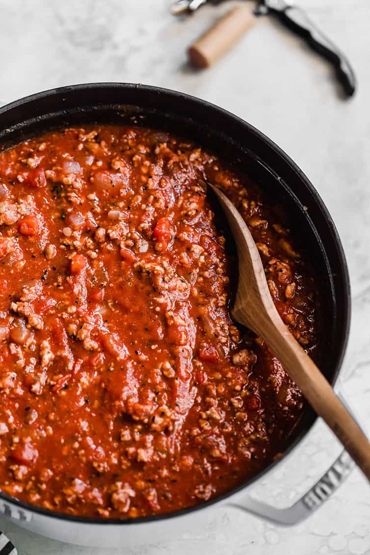 A close up photo of a pot of meat sauce, with a wooden spoon inside.