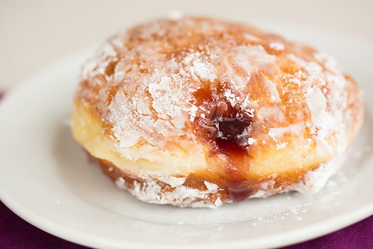A single paczki with fruit filling on a plate.