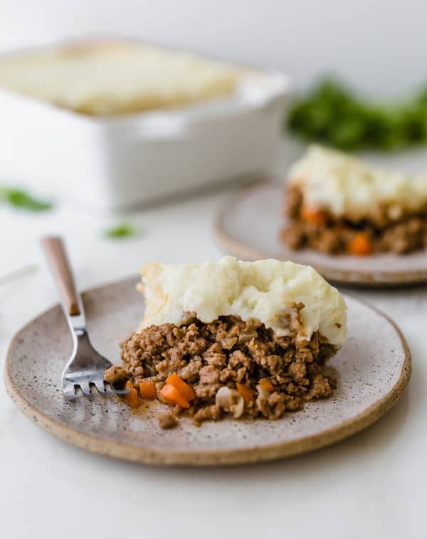 Two plates with shepherd's pie and the casserole dish in the background.