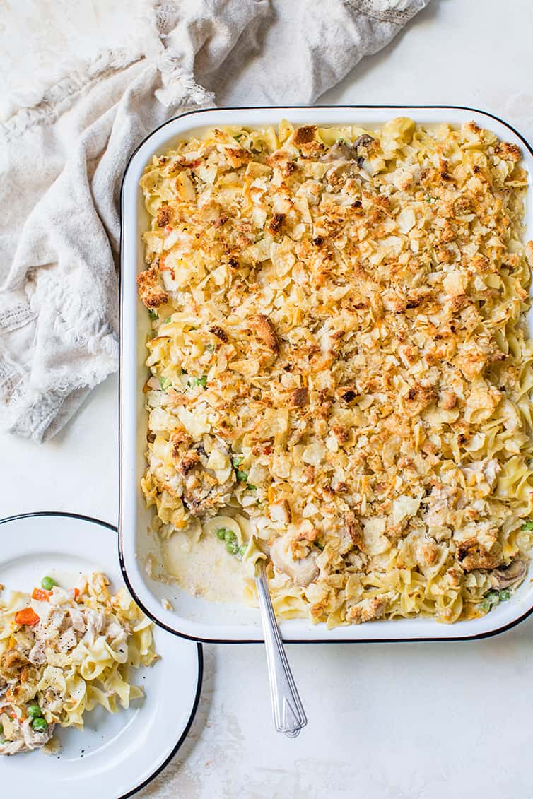 A baking dish of tuna noodle casserole, with a serving scooped onto a plate.