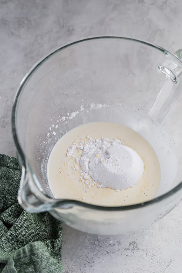 Heavy cream, powdered sugar, and vanilla in a glass mixing bowl.