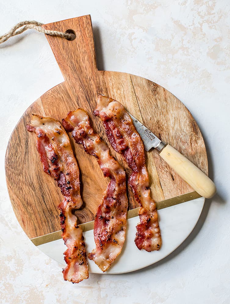 Three slices of bacon on a cutting board.