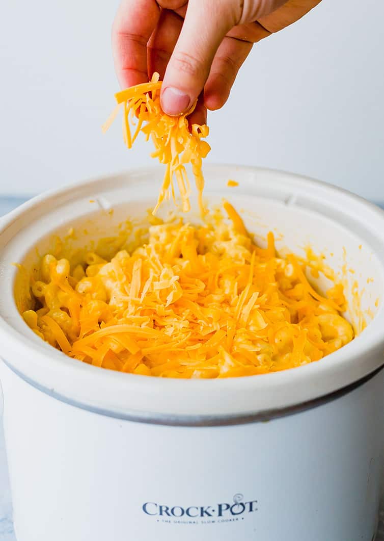 Sprinkling extra cheese on top of macaroni and cheese in the crock pot.
