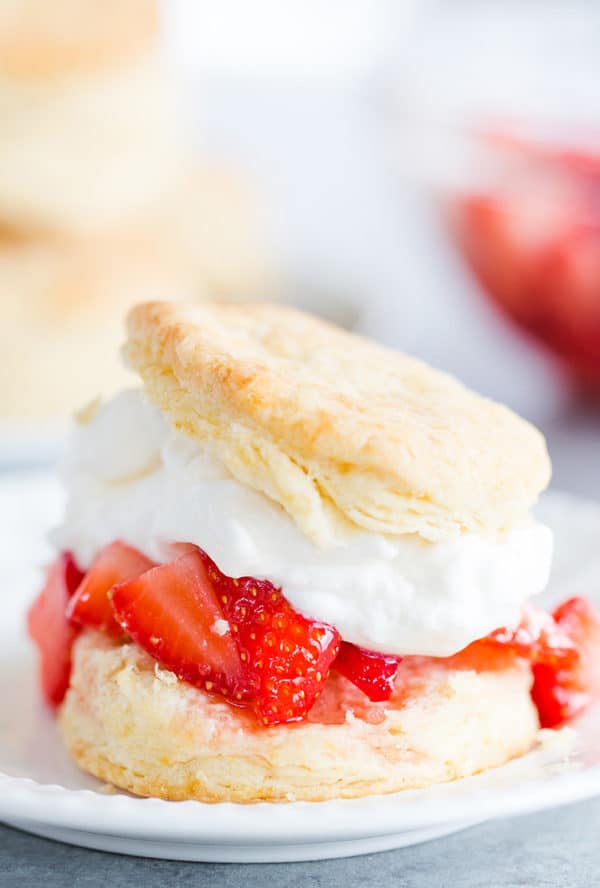 An assembled strawberry shortcake with biscuit, strawberries and whipped cream.