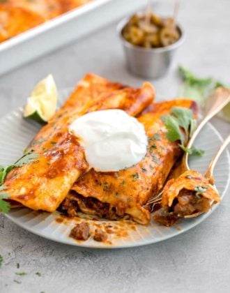 Two beef enchiladas on a plate, with a fork cut into one.