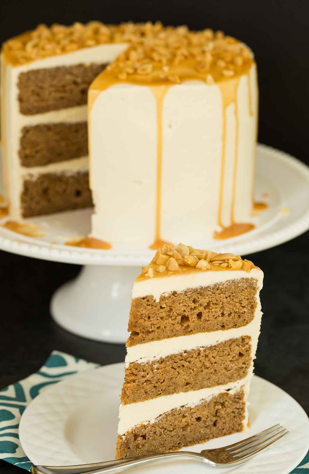 A slice of salted caramel apple cake on a plate with the remaining whole cake on a platter in the background.