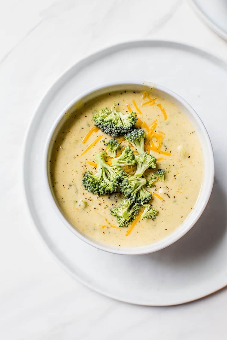 A single bowl of broccoli cheese soup with additional broccoli and shredded cheese on top.