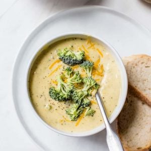 A bowl of broccoli cheese soup with bread on the side.