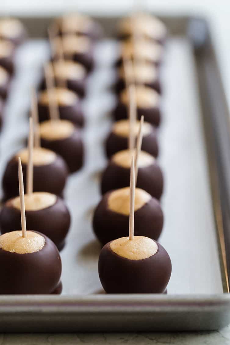 Assembled and dipped buckeyes lined up on a parchment-lined baking sheet.