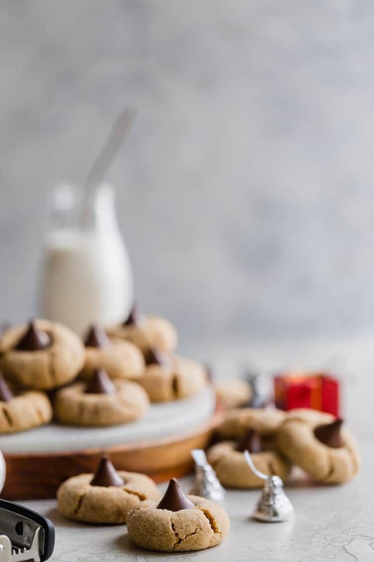 Peanut Butter Blossoms on a tray with a glass container of milk and Hershey's kisses scattered around.