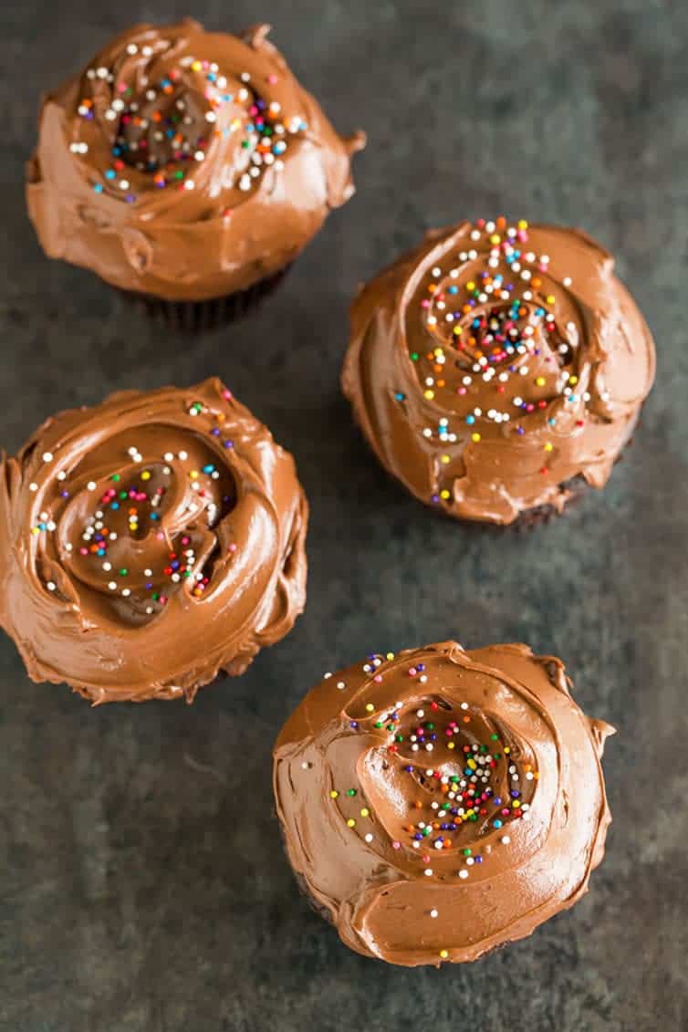 Four chocolate cupcakes with chocolate frosting.