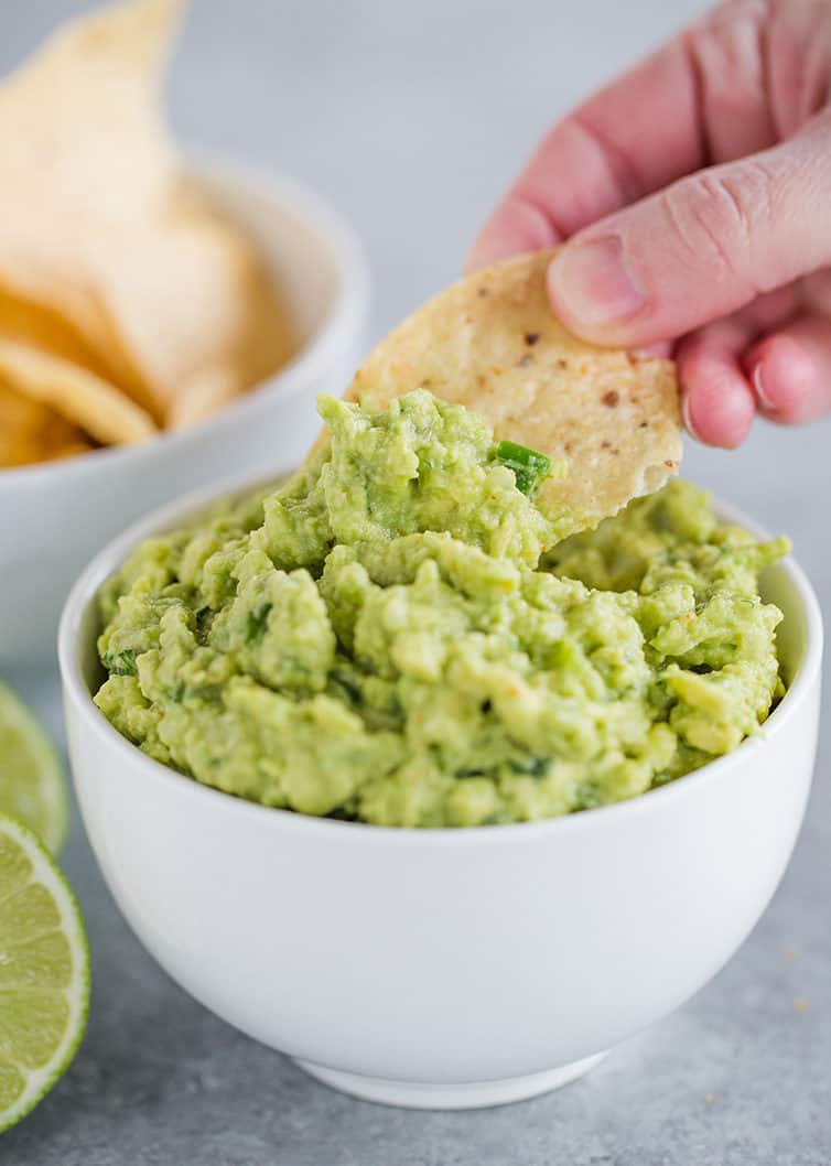 Someone dipping a tortilla chip into a bowl of guacamole.