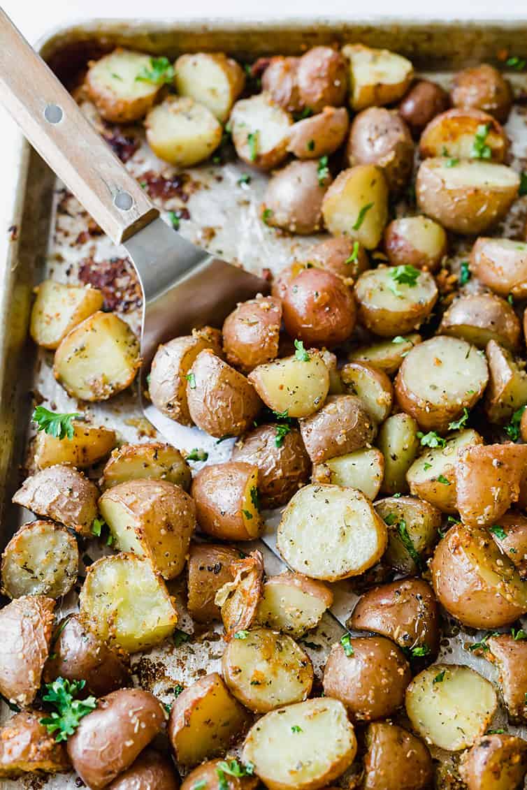 A spatula scooping up roasted red potatoes on a baking sheet.