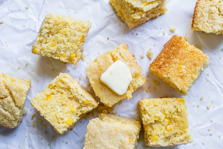 Squares of cornbread on parchment paper, with a pat of butter on top.