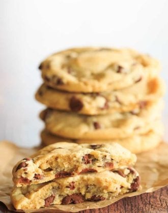 One chocolate chip cookie split in half in front of a stack of cookies.