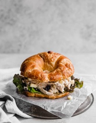 Chicken salad sandwich on a croissant placed on wax paper on a silver plate.