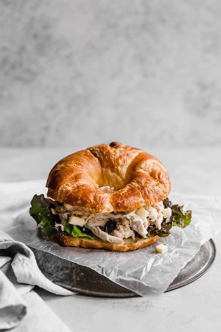 Chicken salad sandwich on a croissant placed on wax paper on a silver plate.