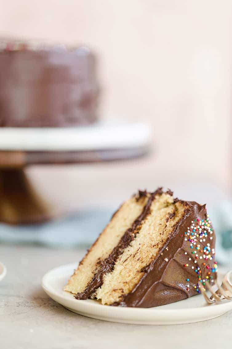 A slice of yellow cake with chocolate frosting on a plate.