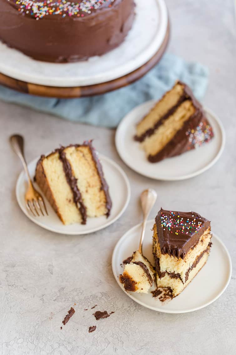 Three slices of yellow cake with chocolate frosting on plates.