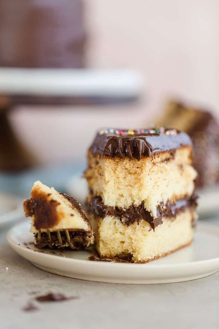 A slice of yellow cake on a plate with a forkful taken out of the front.