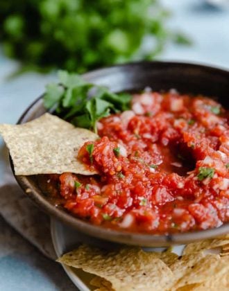 A bowl of salsa with a chip dipped into it.