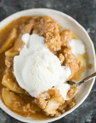 A plate of apple crisp with a scoop of ice cream on top.