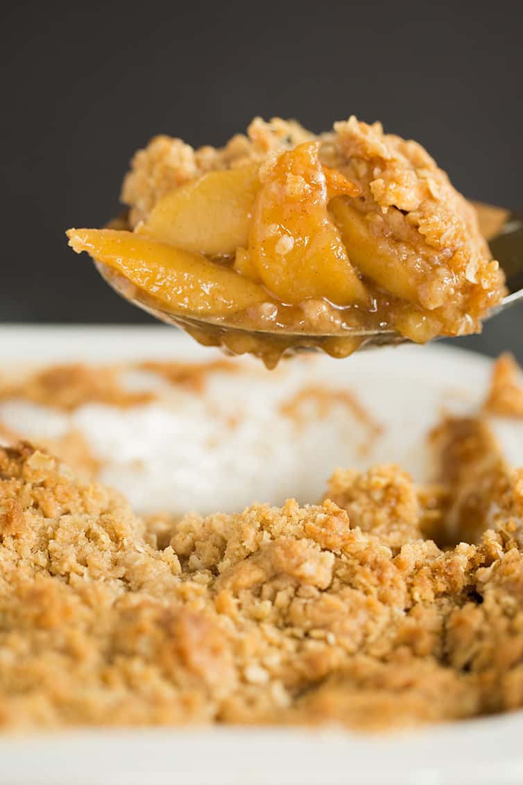 A spoonful of apple crisp being scooped out of the pan.