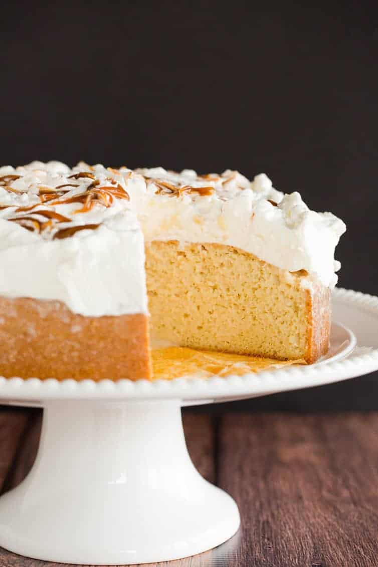Caramel tres leches cake on a cake stand with a slice missing.