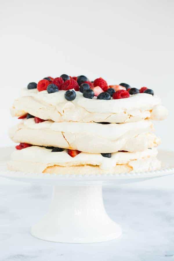 Three layers of pavlova filled and topped with whipped cream and berries.