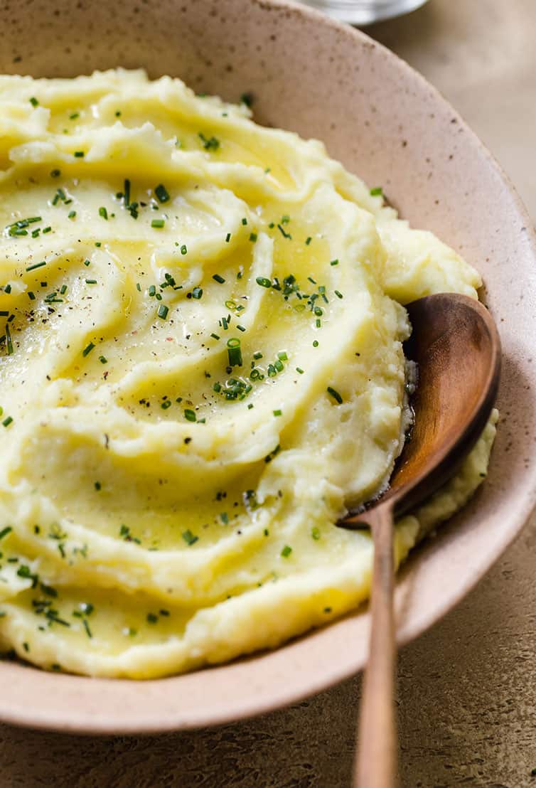 A close-up photo of mashed potatoes swirled in a bowl with a wooden spoon.