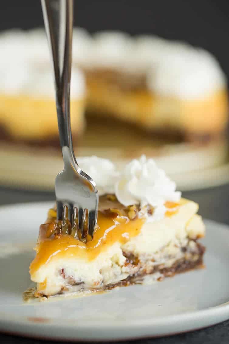A fork going into a slice of pecan pie cheesecake.