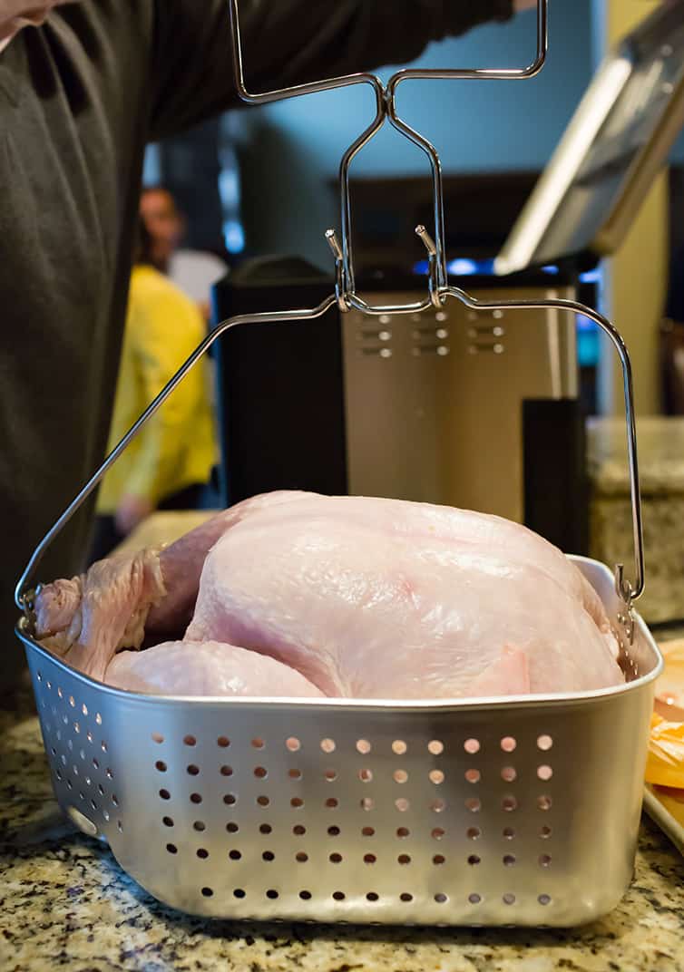 A raw turkey about to be dropped into a deep fryer.
