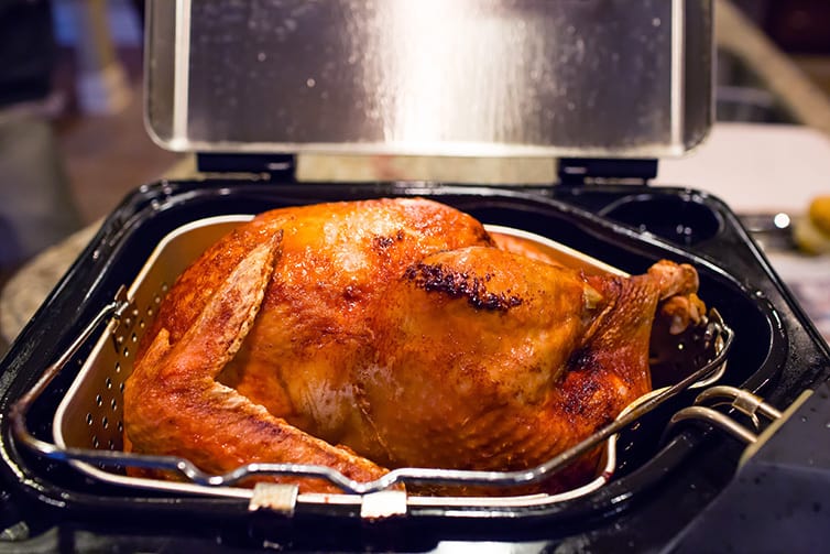 A freshly friend turkey sitting on top of a deep fryer.
