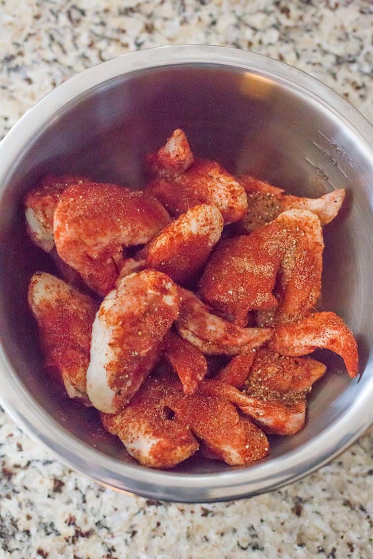Raw chicken wings in a bowl with seasoning.