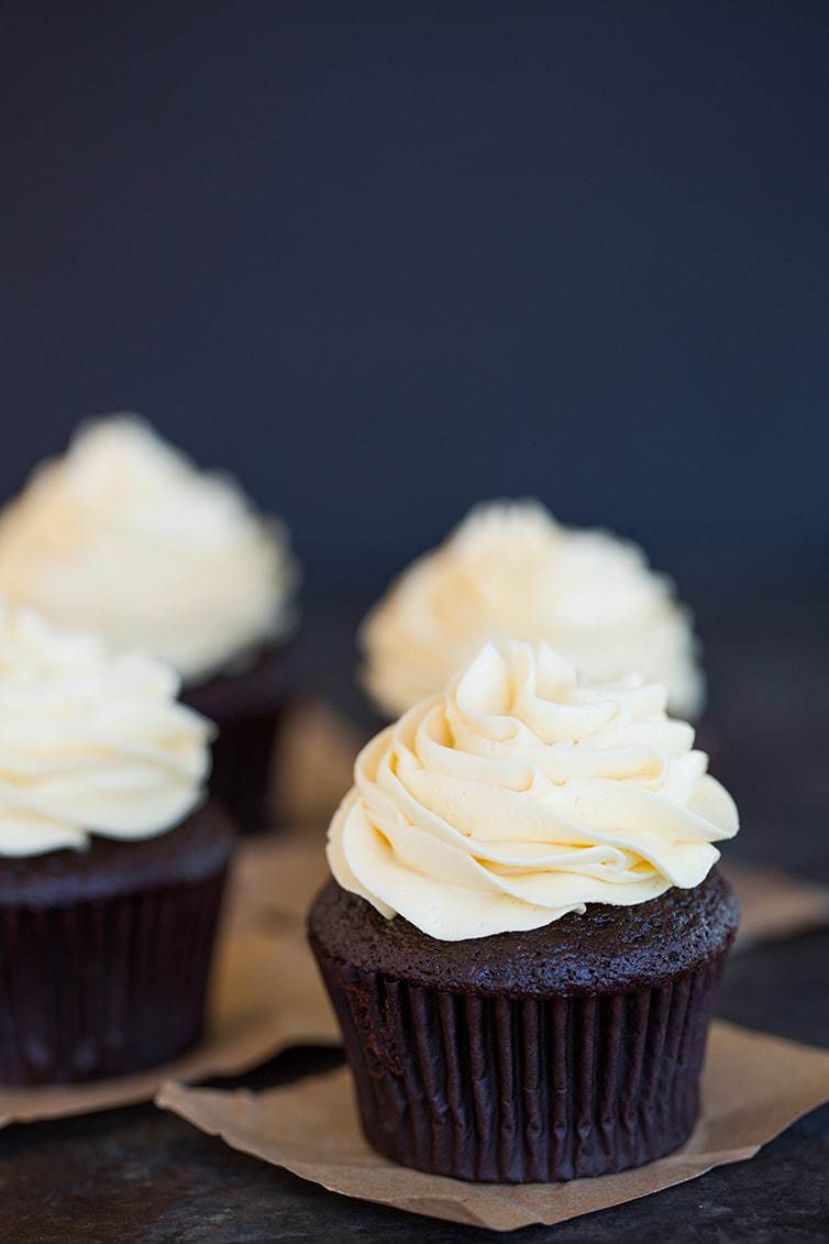 Four chocolate cupcakes with vanilla frosting on butcher paper squares.