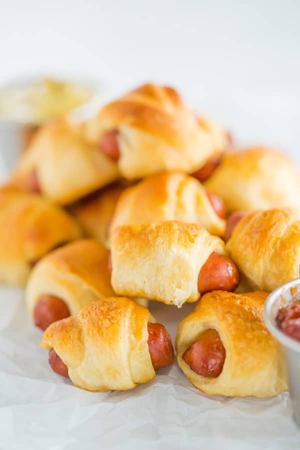 Mini hot dogs wrapped in crescent rolls on parchment paper.